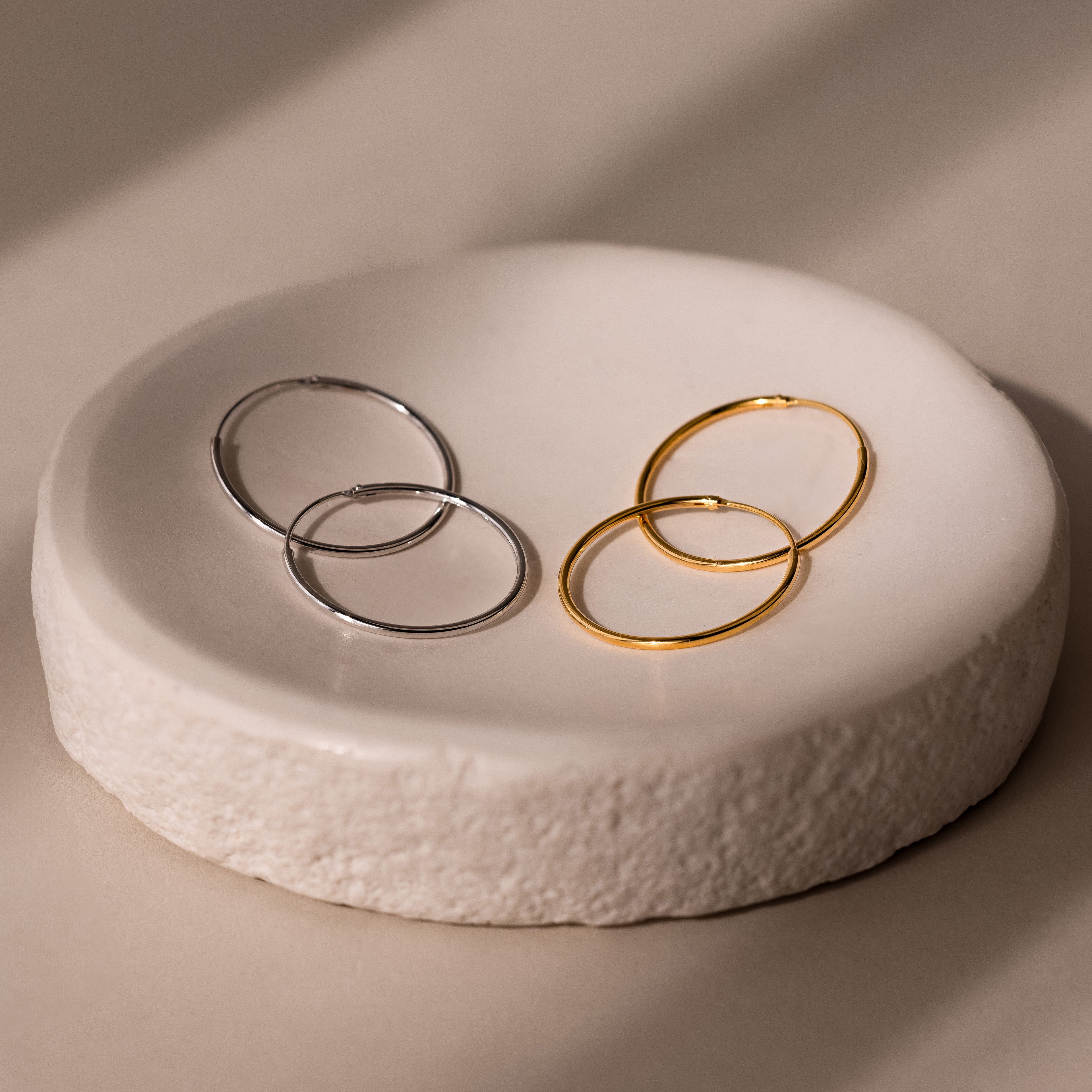 Two pairs of gold and silver hoop earrings on a textured white stone surface.