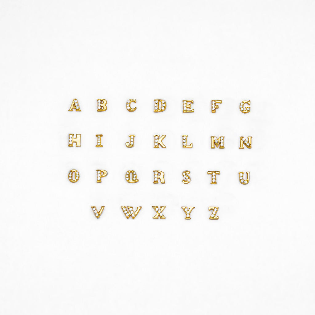 Pave Initial Studs: Gold alphabet letters with rhinestones, arranged in three rows on a white background—ideal as custom initial stud earrings or a unique personalized gift.