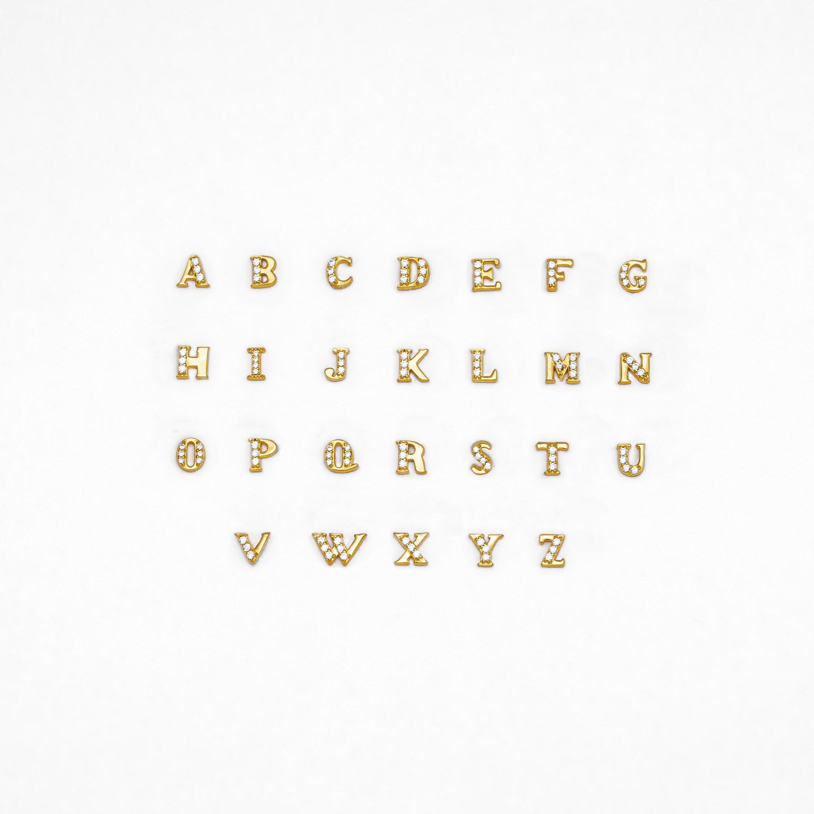 Pave Initial Studs: Gold alphabet letters with rhinestones, arranged in three rows on a white background—ideal as custom initial stud earrings or a unique personalized gift.