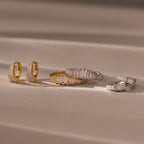 Gold and silver Art Deco Diamond Earrings & Ring Set with rectangular gemstones evoke vintage glamour, elegantly arranged on a soft beige surface with gentle shadows.