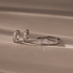 The Art Deco Diamond Earrings & Ring Set in Sterling Silver is displayed on a beige surface with soft lighting.