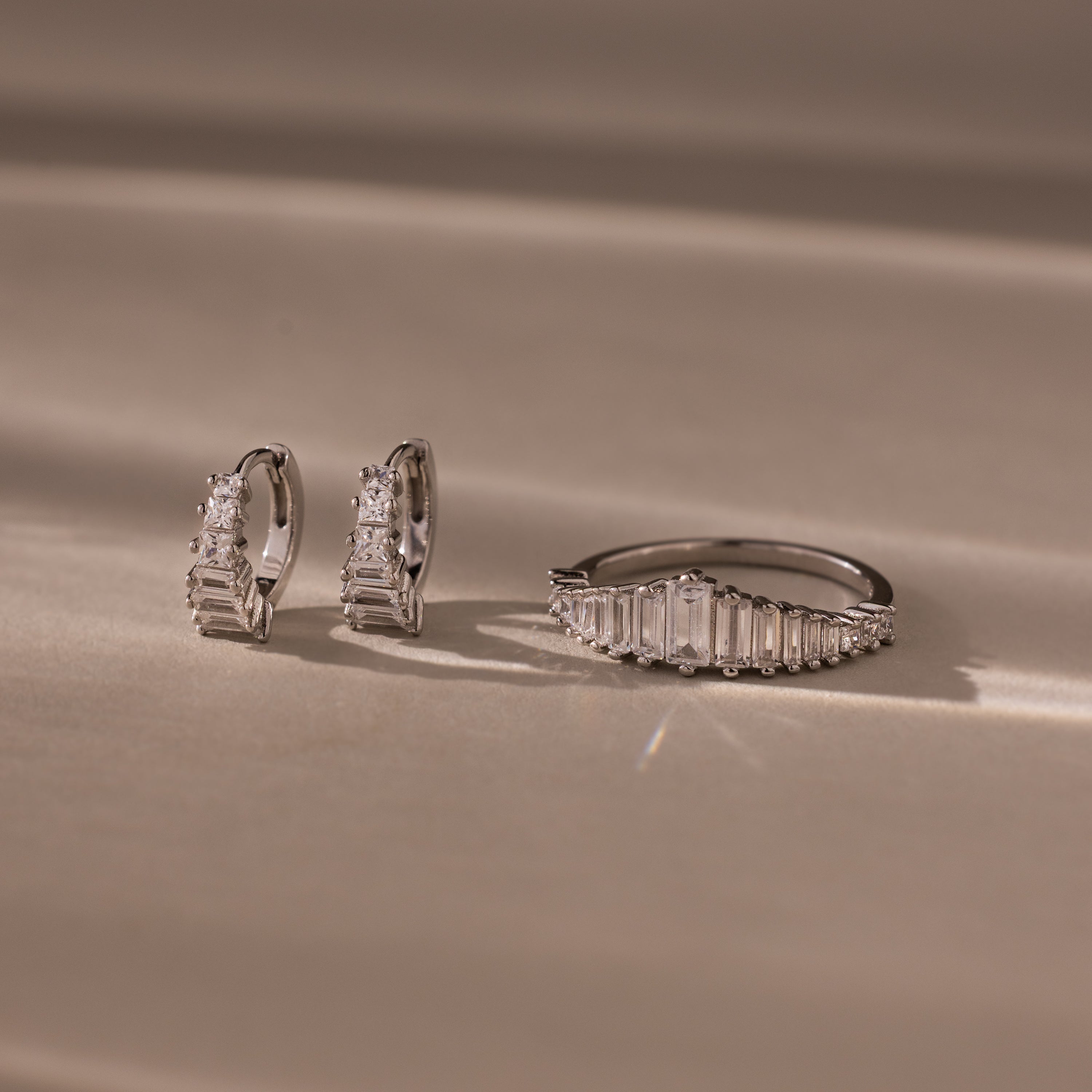 The Art Deco Diamond Earrings & Ring Set in Sterling Silver is displayed on a beige surface with soft lighting.