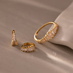 The Art Deco Diamond Earrings & Ring Set in 18K Gold features a gold ring and two hoop earrings with rectangular crystals, displayed on a beige surface to evoke vintage elegance.