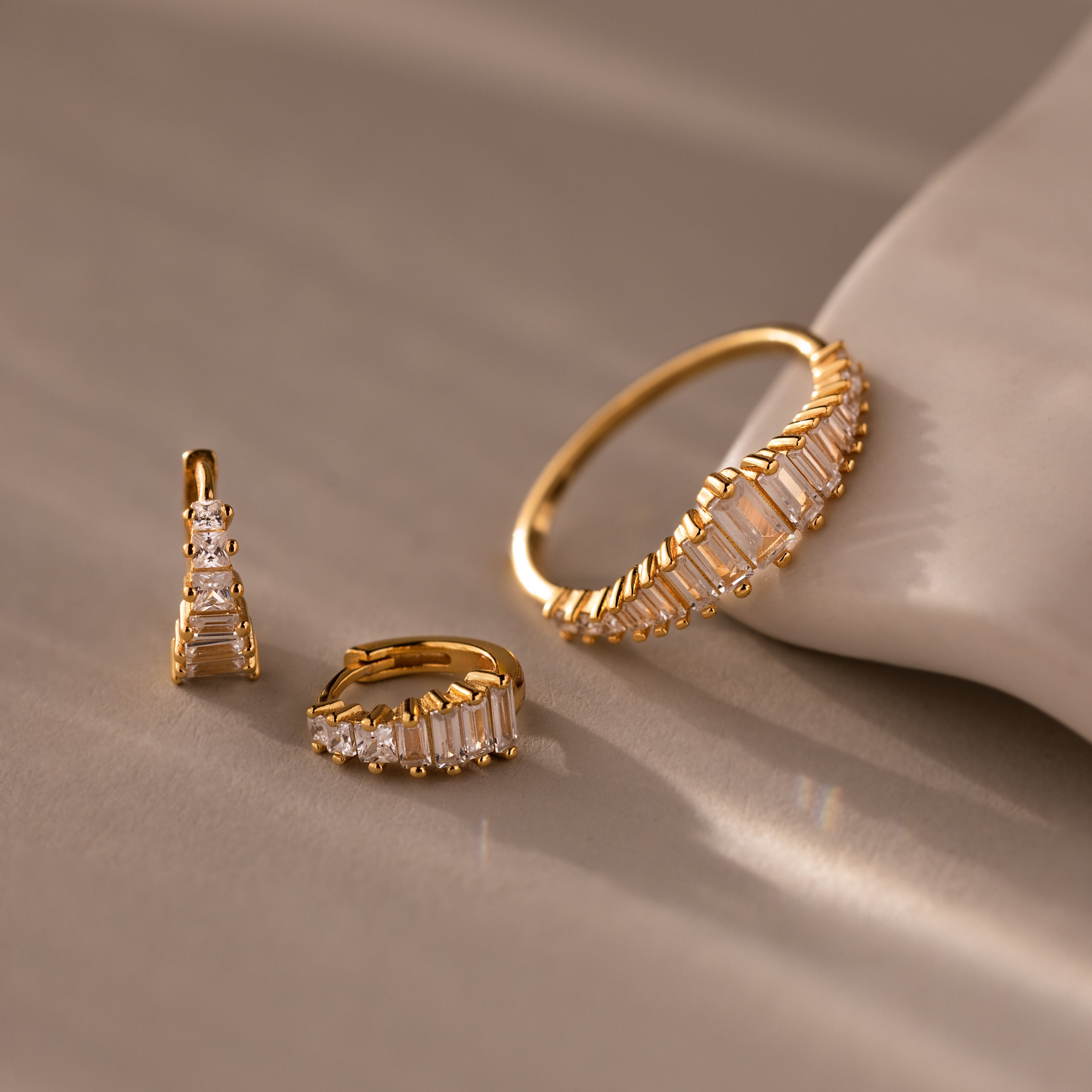 The Art Deco Diamond Earrings & Ring Set in 18K Gold features a gold ring and two hoop earrings with rectangular crystals, displayed on a beige surface to evoke vintage elegance.