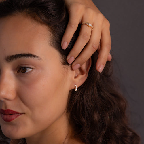 A woman with wavy hair wears the Art Deco Diamond Earrings & Ring Set in 18K Gold, touching her head against a dark background.
