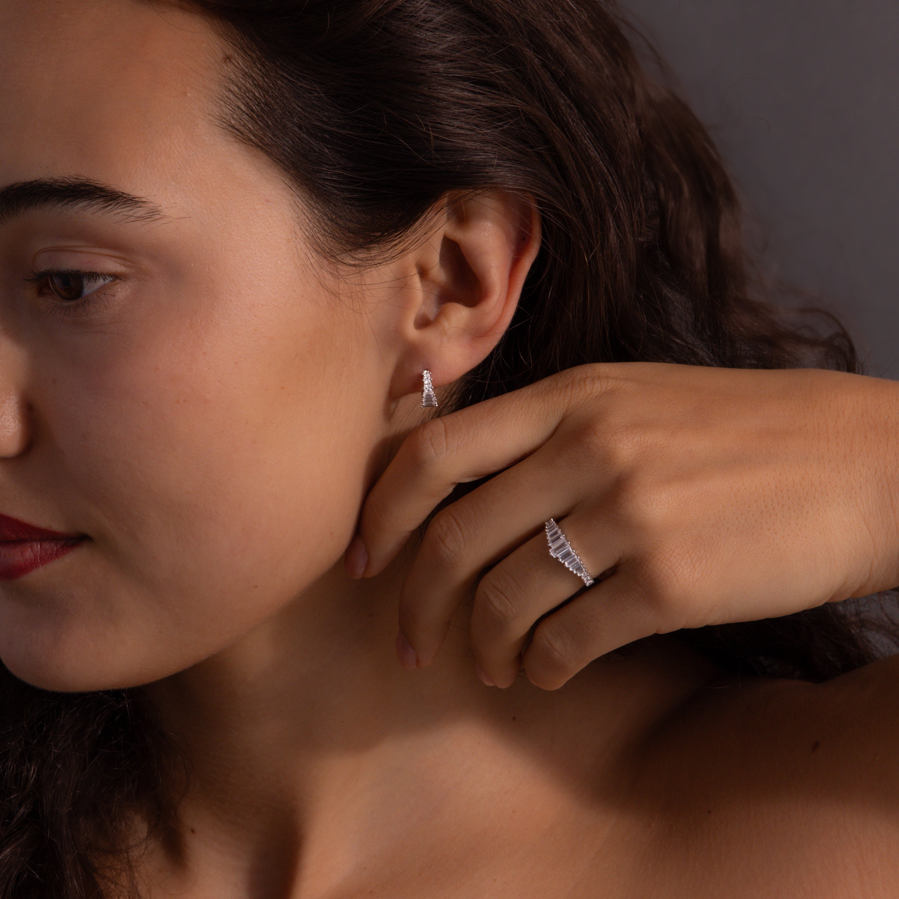 A woman touches her face while wearing the Art Deco Diamond Earrings & Ring Set in Sterling Silver.