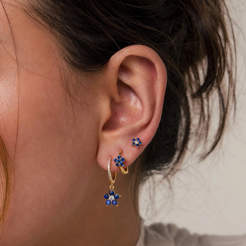 Close-up of a woman's ear adorned with the Sapphire Flower Earrings Set, featuring three gold earrings with blue sapphire flower designs—an elegant option for lovers of unique gemstone jewelry.