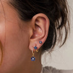 Close-up of a woman's ear adorned with the Sapphire Flower Earrings Set, featuring three gold earrings with blue sapphire flower designs—an elegant option for lovers of unique gemstone jewelry.