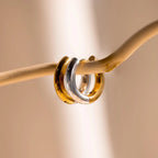 Mixed Metal Chunky Hoops are shown hanging on a curved beige branch, highlighting their chic design against a softly blurred background.