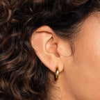 Close-up of a person’s ear wearing Mixed Metal Chunky Hoops, framed by curly brown hair.