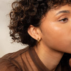 Close-up of a woman with curly hair wearing Mixed Metal Chunky Hoops and a sheer brown top.