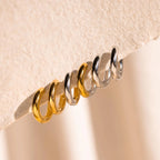 Three Mixed Metal Chunky Hoops in gold and silver are displayed on a textured beige surface, highlighting the stylish two-tone design of these hoop earrings.