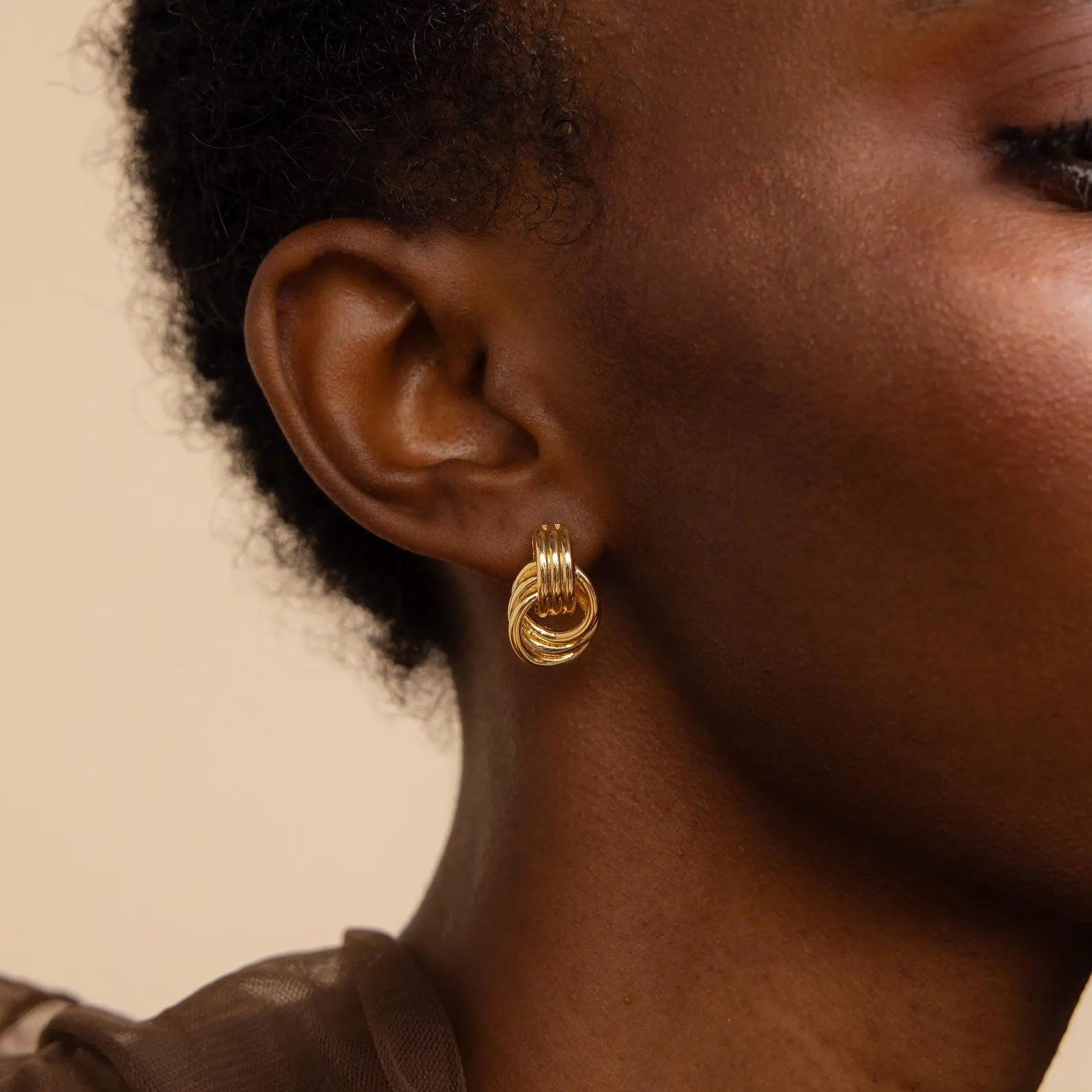 Close-up of a person wearing the Mixed Metal Mini Triple Knot Earrings, featuring gold multi-hoop design against a neutral background, highlighting their everyday luxury appeal.