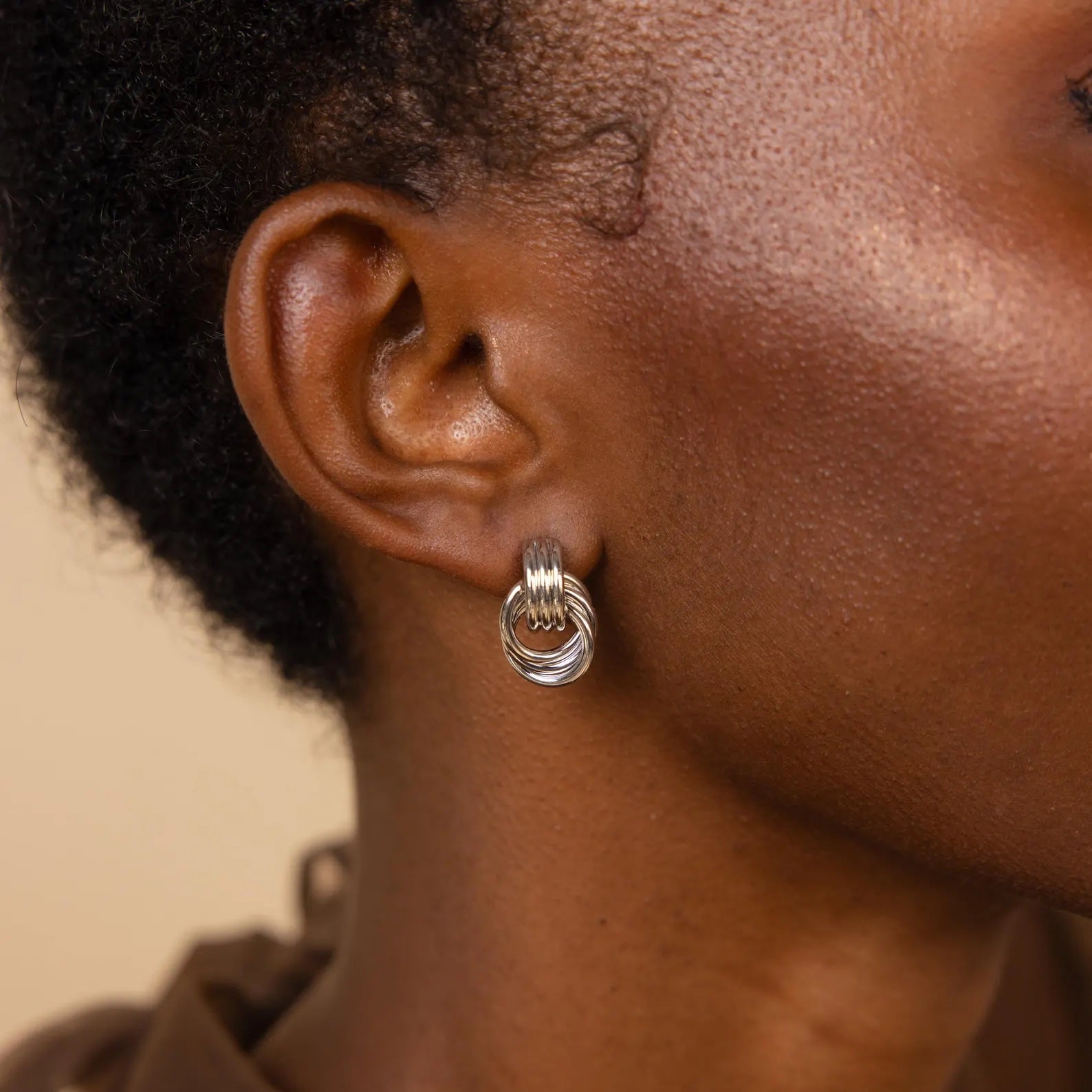 Close-up of a person wearing Mixed Metal Mini Triple Knot Earrings against a neutral background, capturing the essence of everyday luxury.