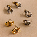 The Mixed Metal Mini Triple Knot Earrings—six gold and silver knot-shaped studs—are styled on a textured beige surface, offering a touch of everyday luxury to your collection.