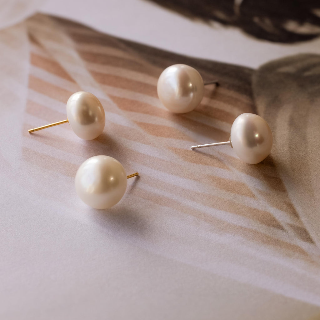 Bold Pearl Studs—featuring four elegant pearl studs with gold and silver posts—are displayed on a soft, striped surface, perfect for those who appreciate timeless jewelry.