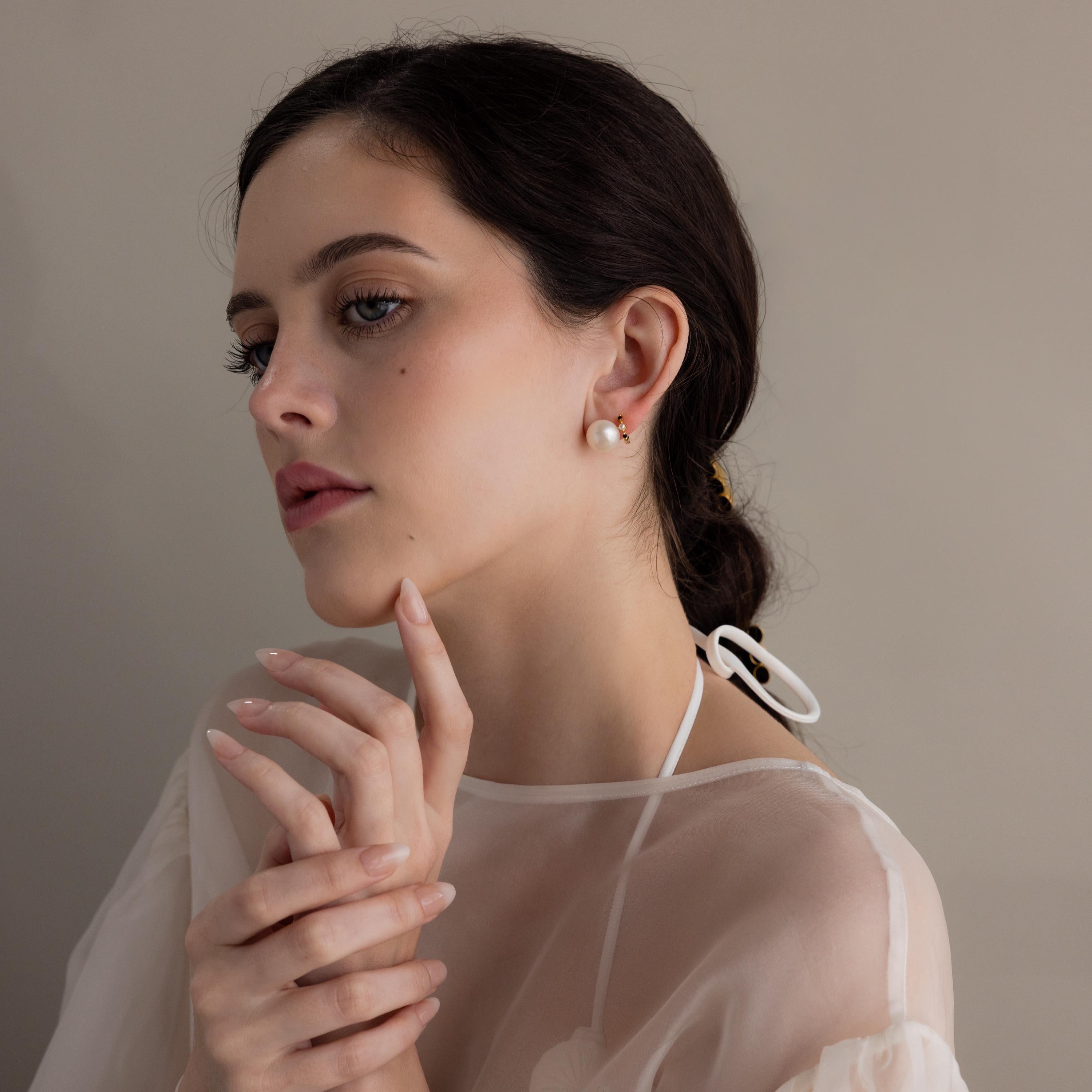Woman with dark hair in a low bun, wearing Bold Pearl Studs and a sheer white top, posed thoughtfully.