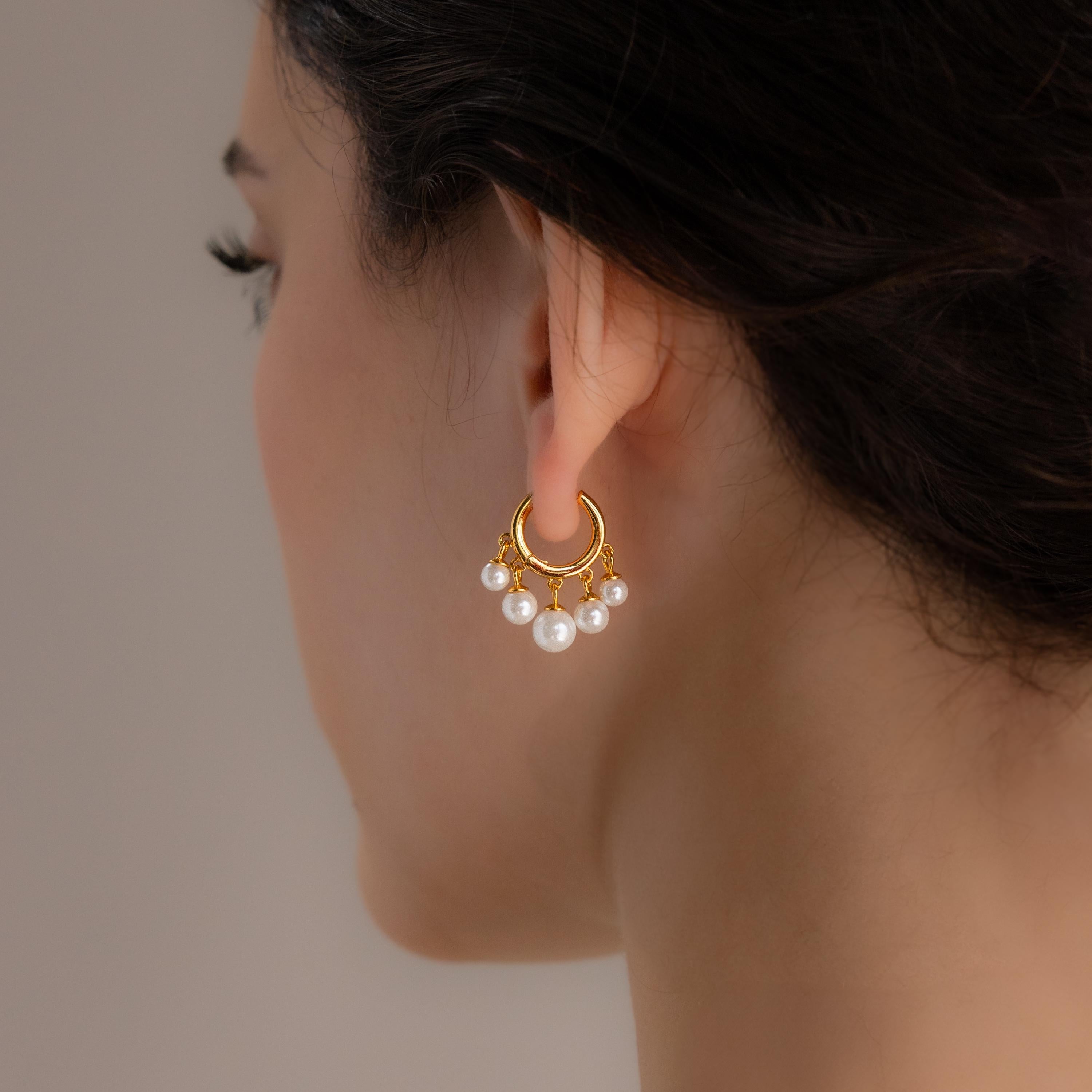 A woman is shown from the side wearing Pearl Chandelier Huggies—gold hoops with hanging white pearl beads—against a neutral background.