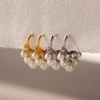 Two pairs of Pearl Chandelier Huggies, featuring gold and silver hoop earrings adorned with pearl beads, are elegantly displayed on a white surface.