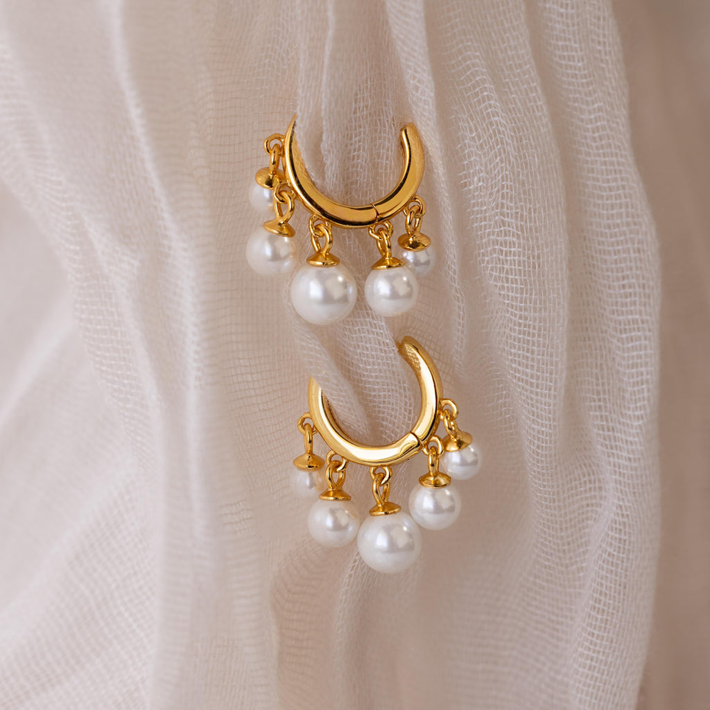 Pearl Chandelier Huggies with gold crescent design and dangling pearl beads, showcased on a soft, sheer beige fabric background.