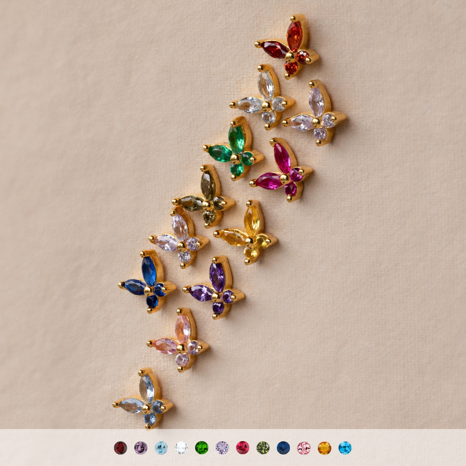 Twelve Butterfly Birthstone Flatback Studs with colorful gemstones are arranged diagonally on a beige background, adding a delightful personalized touch to your jewelry collection.
