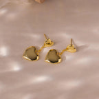 Duo Heart Drop Studs with a shiny gold finish, elegantly displayed on a soft, light-colored surface.