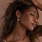 Woman with closed eyes touches her hair, showcasing Duo Heart Drop Studs earrings against a neutral background.