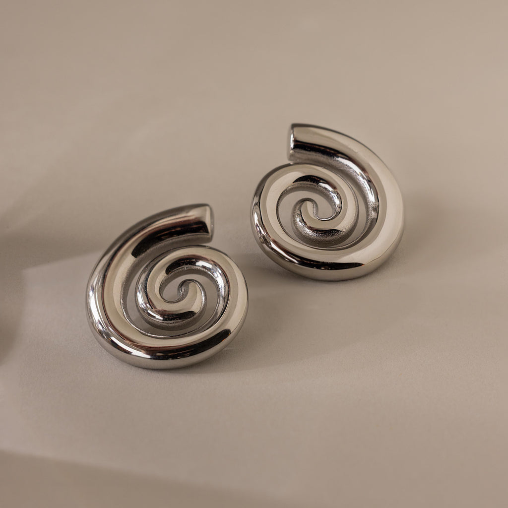 A pair of Bold Spiral Stud Earrings in shiny silver is displayed on a plain, light-colored background.