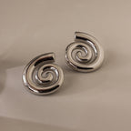 A pair of Bold Spiral Stud Earrings in shiny silver is displayed on a plain, light-colored background.