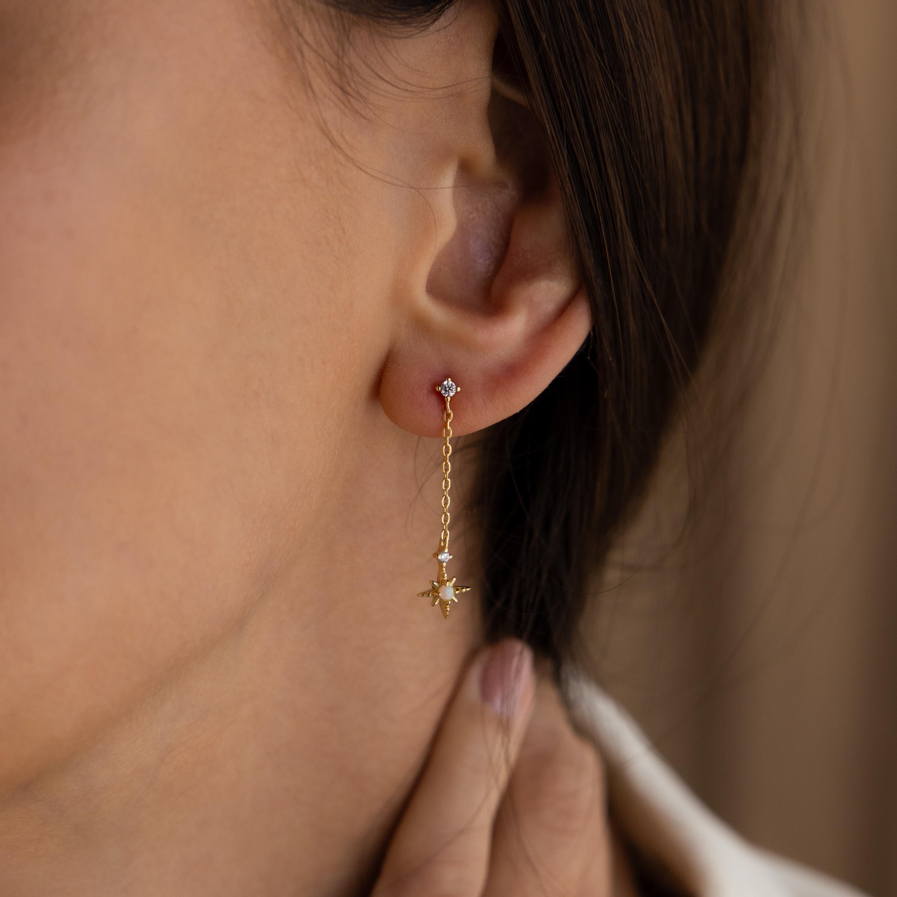 Model wearing gold Starburst Chain Stud Earrings. It is a diamond stud with a dangling chain, then an opal starburst charm hanging from the chain.
