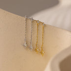 Close up of a pair of silver starburst chain stud earrings and a pair of gold starburst chain stud earrings hanging side by side on a ceramic dish.