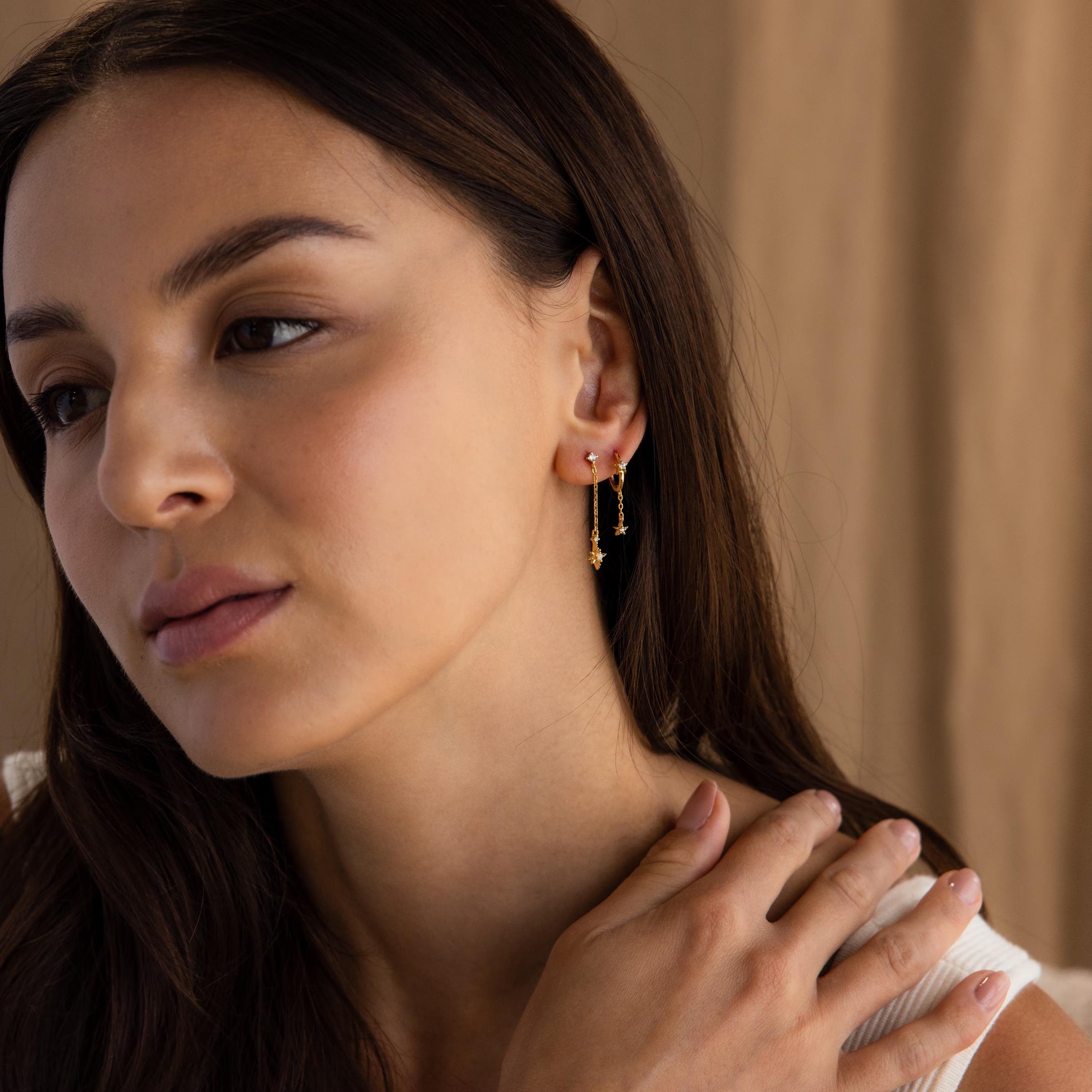 Posed far shot of model wearing a gold starburst chain stud earrings, accompanied by another star earring on a second piercing.