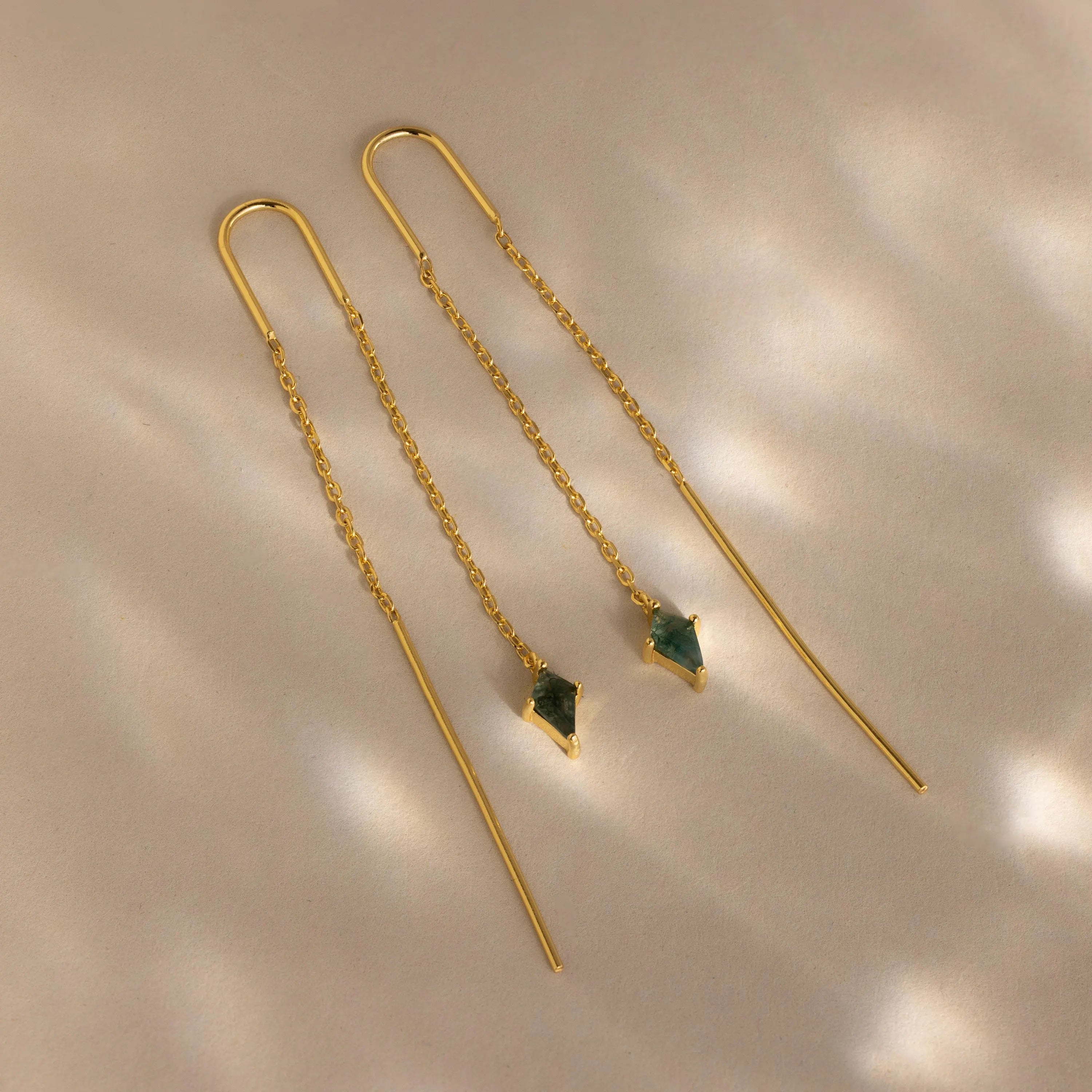 Agate Threader Earrings featuring delicate chains and green moss agate gemstone pendants are displayed on a beige surface for a modern, elegant look.