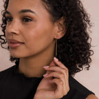 Woman with curly hair wearing a black top, looking to the side while holding Agate Threader Earrings.