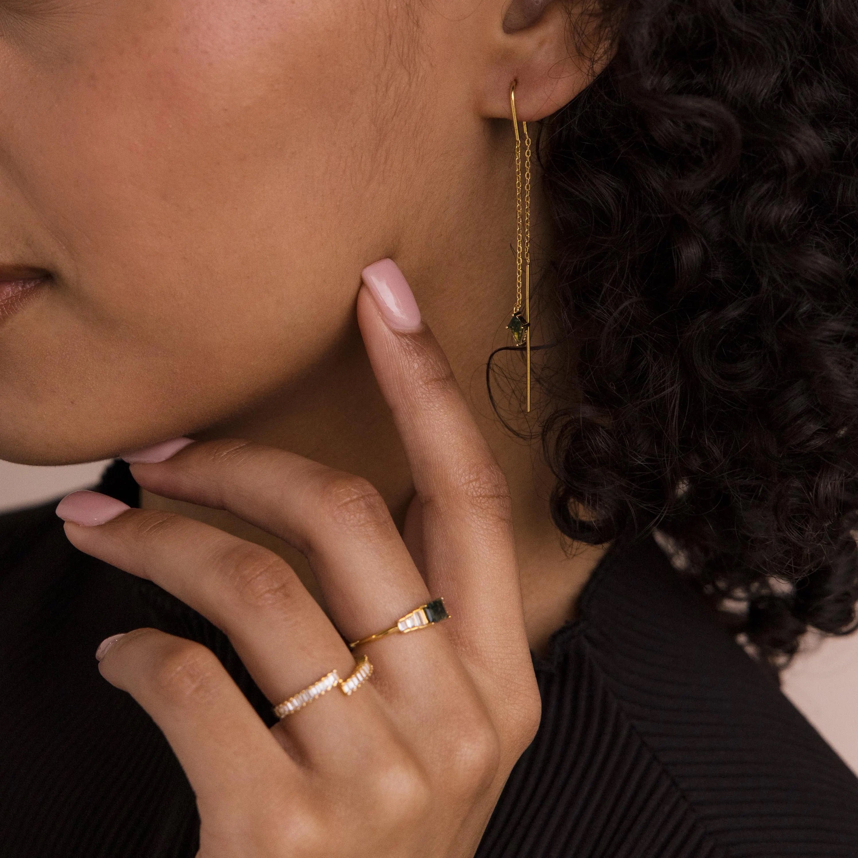 Woman with curly hair wears Agate Threader Earrings, touching her face with manicured nails and showcasing modern style.
