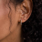 Close-up of a person’s ear wearing Pave Pearl Huggies—small gold hoops featuring sparkling stones and delicate pearls.