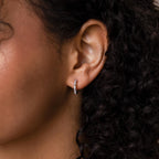 Close-up of a person’s ear adorned with Pave Pearl Huggies, curls of dark hair framing the elegant earrings.