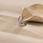 Two Pave Pearl Huggies rest beside a speckled ceramic dish on a beige surface.