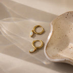 Opal Marquise Huggies featuring small opal charms are displayed next to a speckled ceramic dish on a beige surface, bringing an elegant touch to any setting.