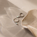 Two Opal Marquise Huggies are placed next to a speckled ceramic dish on a beige surface.