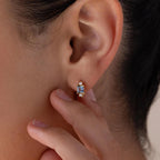 A close-up of someone touching the Aquamarine Pearl Huggies on their ear, highlighting this elegant bridal jewelry.