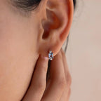 A close-up of a person wearing Aquamarine Pearl Huggies, touching their ear with their fingers.