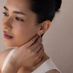 A woman with her hand on her face wears elegant Aquamarine Pearl Huggies, the perfect earrings for bridal jewelry or weddings.