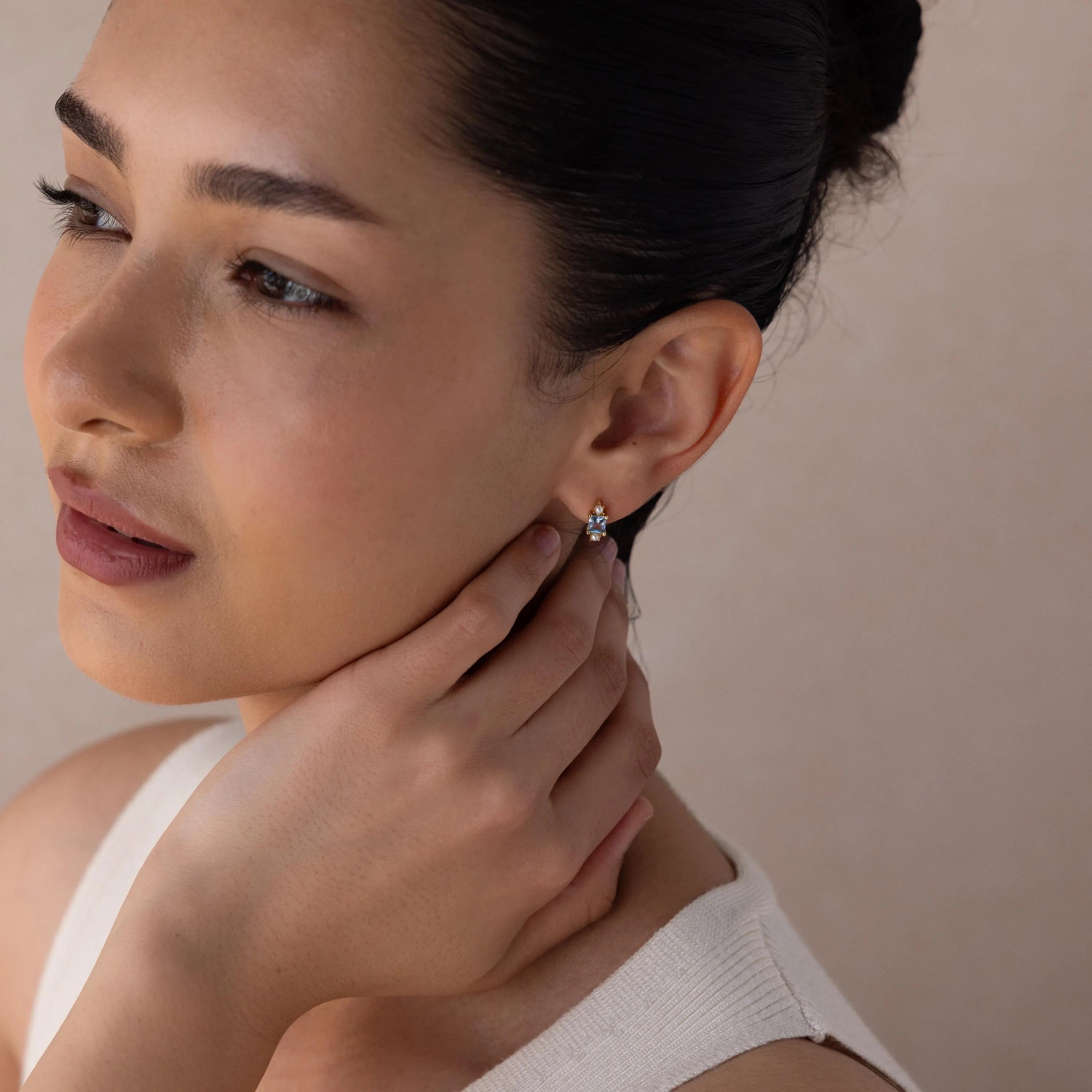 A woman with her hand on her face wears elegant Aquamarine Pearl Huggies, the perfect earrings for bridal jewelry or weddings.