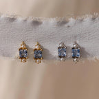 Two pairs of Aquamarine Pearl Huggies—ideal as bridal or wedding earrings—are displayed on frayed white fabric; one pair in gold, the other in silver.