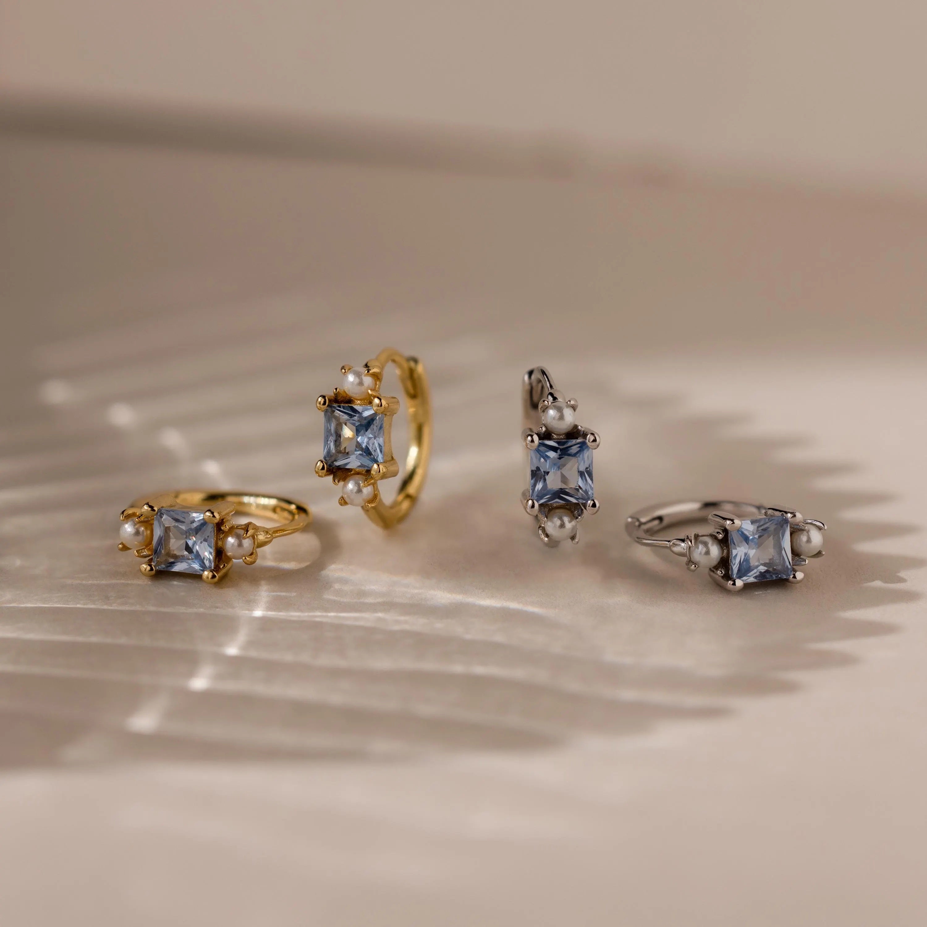 Two pairs of Aquamarine Pearl Huggies, one in gold and one in silver, displayed on a textured surface—perfect bridal earrings to accent your special day.