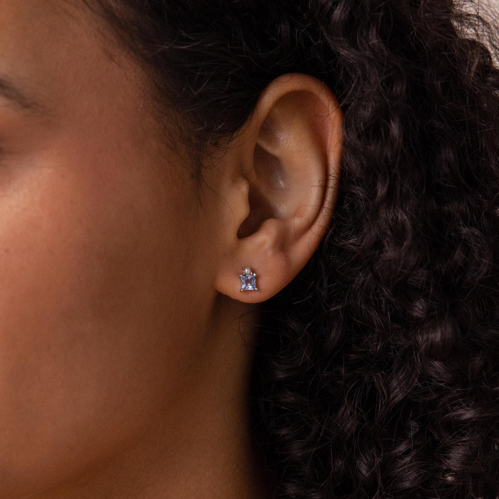 Close-up of a woman's ear with curly dark hair, wearing small, silver Aquamarine Pearl Studs.