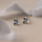 Aquamarine Pearl Studs: A pair of silver bridal stud earrings with princess-cut light blue gemstones, showcased on a soft beige background.