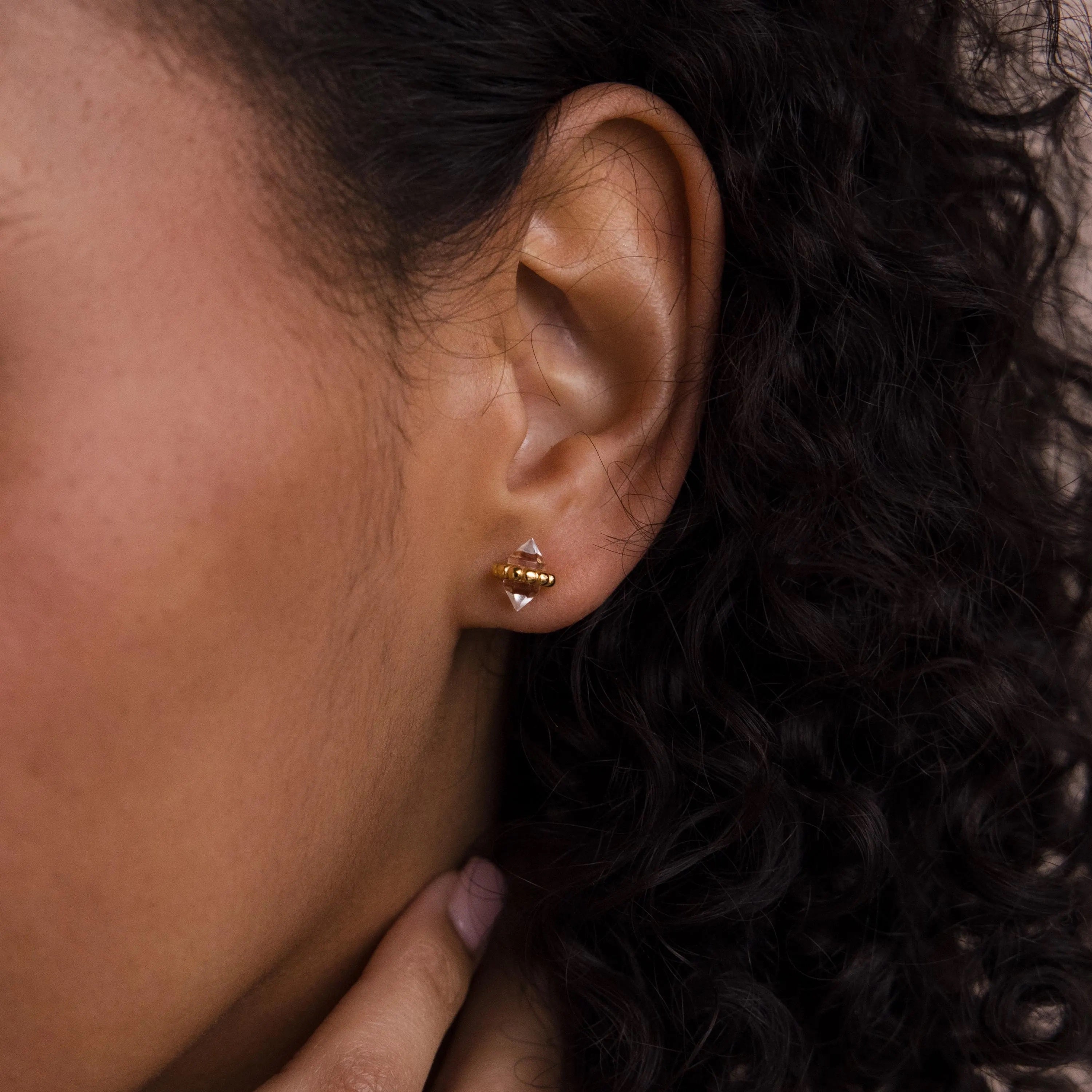 A close-up of a person’s ear adorned with Beaded Herkimer Studs as their hand touches curly dark hair.