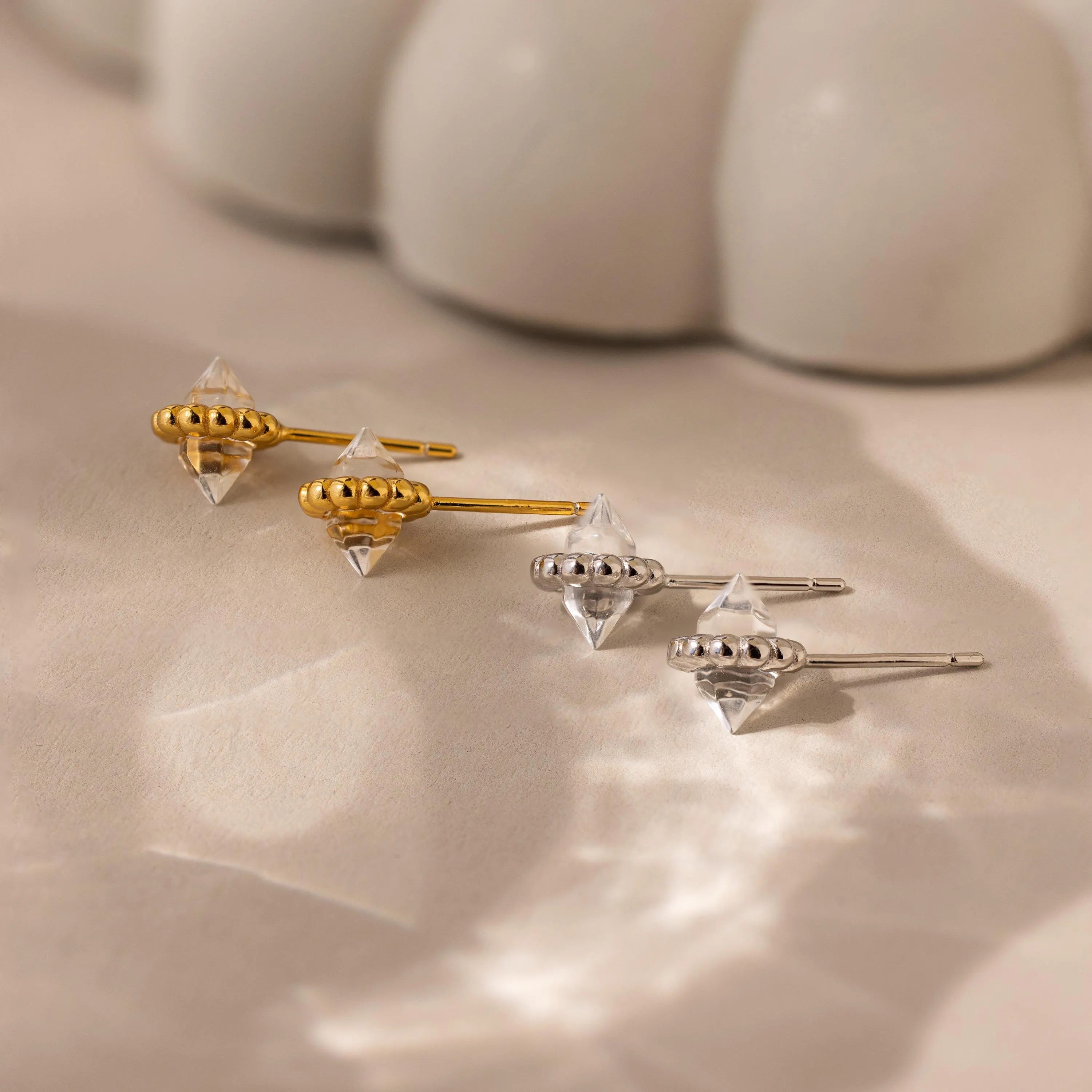 Two pairs of Beaded Herkimer Studs earrings—one gold, one silver—are displayed on a light surface with soft shadows, showcasing their luminous brilliance.